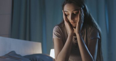 Stressed young woman suffering from insomnia, she is sitting on the bed and thinking