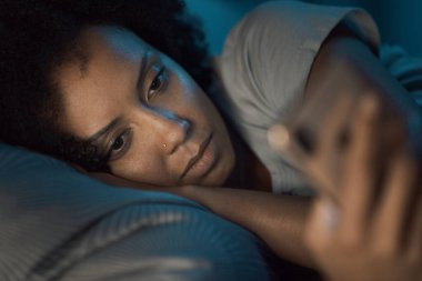 Sleepless woman lying in bed at night and connecting online using her smartphone