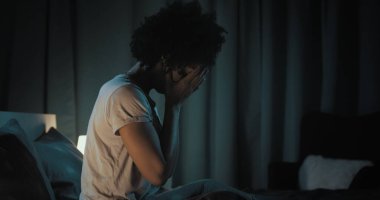Üzgün Afro-Amerikan kadın yatakta oturuyor, uykusuzluk çekiyor.
