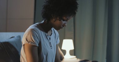 Sad african american woman sitting on bed at night, she can't sleep