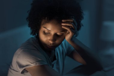 Sleepless african american woman sitting in bed at night, she is stressed and unable to sleep