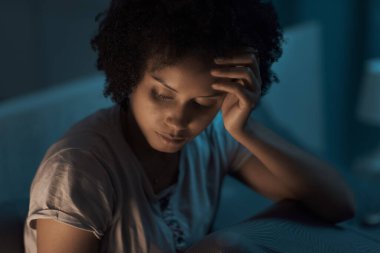 Sleepless african american woman sitting in bed at night, she is stressed and unable to sleep