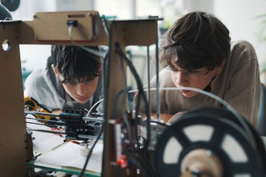 Kids learning 3D printing in the lab, the are staring at the 3D printer printing their prototype