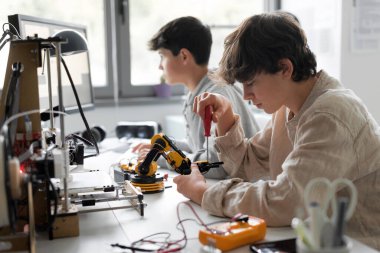 Young students using a 3D printer in the lab at school, one is using a screwdriver