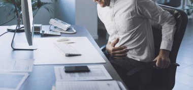 Businessman sitting at office desk and having stomach ache, he is touching his belly with his hand