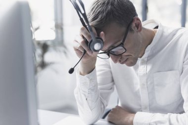 Exhausted office worker sitting at desk, he is tired and having a headache, job burnout concept