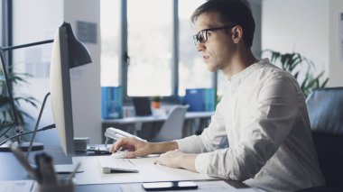 Young corporate businessman sitting at desk and working with his computer, he is focused and staring at the computer screen