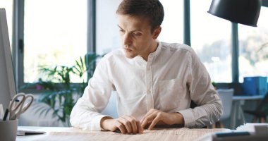 Man sitting at desk in the office and reading a newspaper, he is focused and thinking