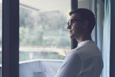 Confident young businessman standing next to a window and looking away