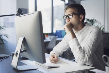 Professional businessman sitting at desk and working with his computer, he is looking at the screen and thinking