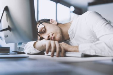 Lazy office worker sleeping at his desk, he is exhausted and stressed