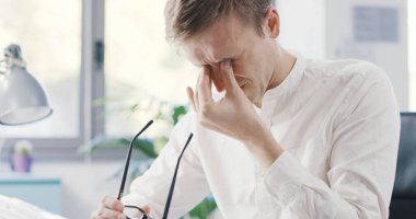 Stressed tired businessman sitting at desk and touching his eyes