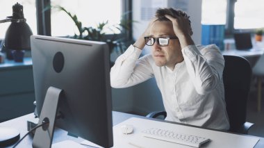 Panicked businessman sitting at desk and staring at the computer screen, system failure and computer problems concept