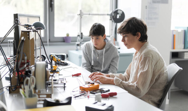 Students sitting at desk in the lab and learning 3D printing together, one is typing and the other is assisting him