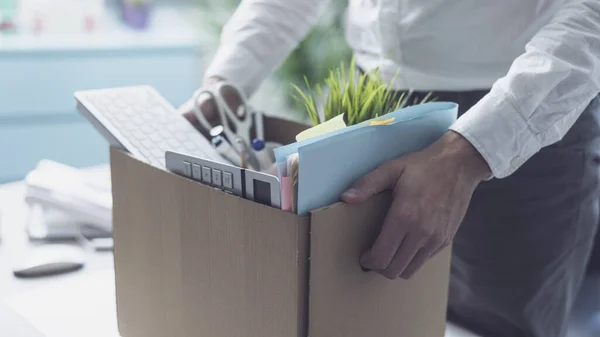 Fired office worker packing his belongings in a cardboard box and leaving the office, crisis and unemployment concept