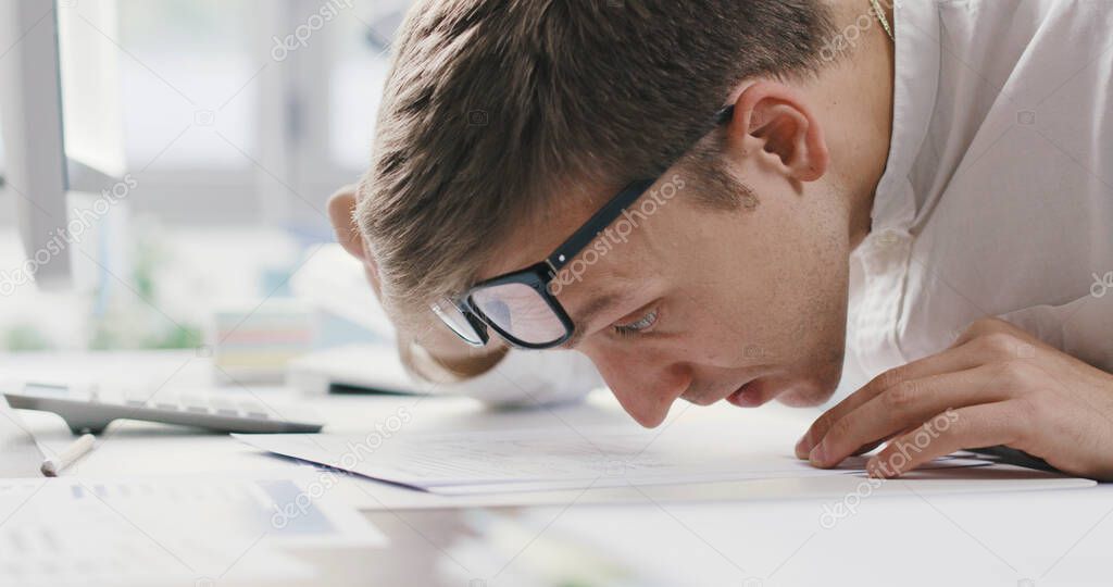 Corporate office worker having vision problems, he gets very close to a document to read the text