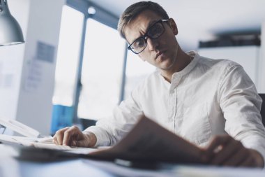 Man sitting at desk in the office and reading a newspaper, he is focused and thinking