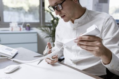 Office worker cutting the telephone cord with scissors, he is tired of receiving phone calls