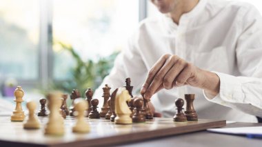 Man sitting at desk and playing chess, he is moving a piece on the chessboard