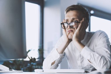 Insane stressed office worker having a nervous breakdown, he is sitting at desk with head in hands, job burnout concept