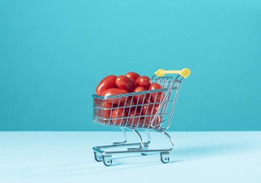 Tiny shopping cart full of fresh tomatoes, grocery shopping and fresh food concept