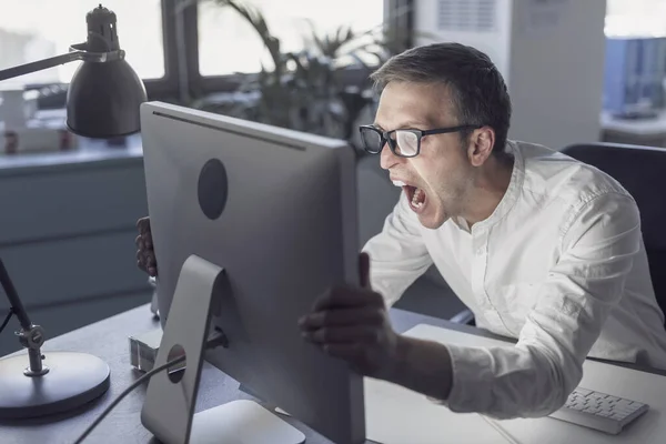 Angry office worker sitting at desk and shouting at the computer, system failure concept