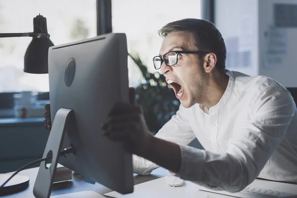 Angry office worker sitting at desk and shouting at the computer, system failure concept