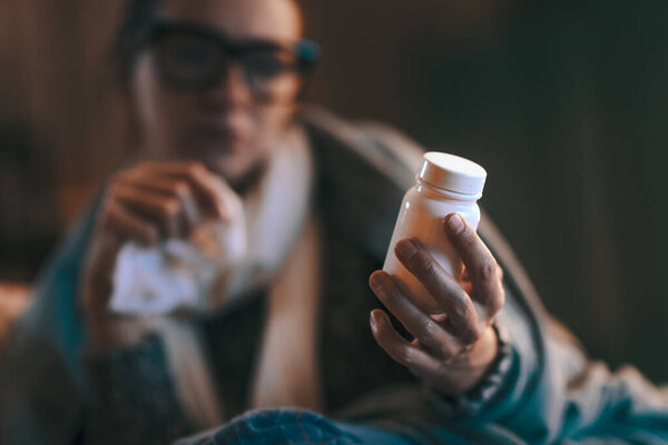 Sick woman with cold and flu at home, she is holding a pill bottle and checking medicine information