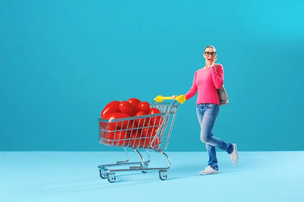 Tiny happy woman pushing a miniature shopping cart full of tomatoes