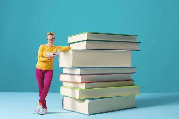 Tiny smart woman leaning on a pile of books and reading, education and learning concept