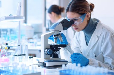 Young scientists conducting research investigations in a medical laboratory, a researcher in the foreground is using a microscope