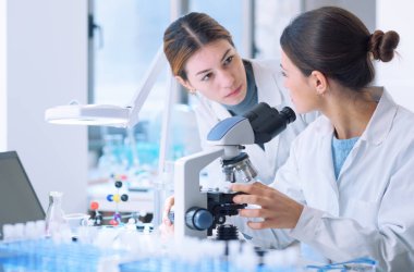 Young female researchers working together in a medical lab, they are examining samples with a microscope