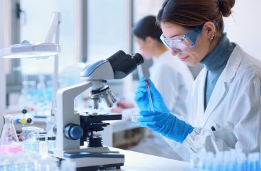 Young female student in the research lab, she is examining a sample in a petri dish and using the microscope