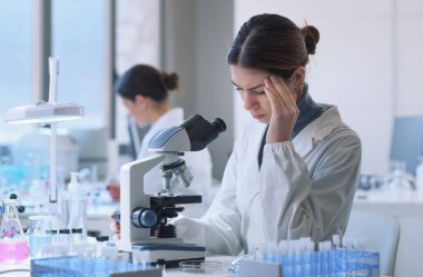 Young researcher working in the lab and using a microscope, she is having a headache