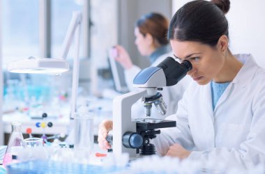 Students doing research in the clinical laboratory, a researcher is using a microscope in the foreground, scientific research concept