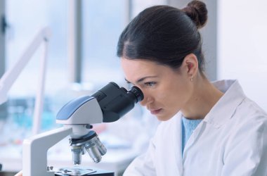 Students working in the clinical laboratory, a researcher is using a microscope in the foreground, scientific research concept