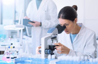 Students working in the clinical laboratory, a researcher is using a microscope in the foreground, scientific research concept