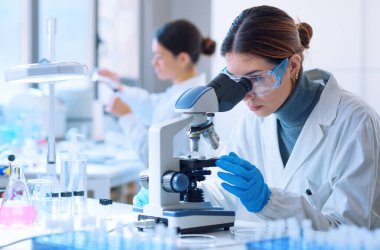 Young scientists conducting research investigations in a medical laboratory, a researcher in the foreground is using a microscope