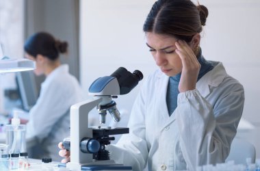 Young researcher working in the lab and using a microscope, she is having a headache