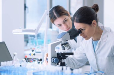 Young female researchers working together in a medical lab, they are examining samples with a microscope