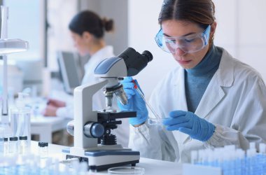 Young female student in the research lab, she is examining a sample in a petri dish and using the microscope