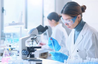 Young female student in the research lab, she is examining a sample in a petri dish and using the microscope