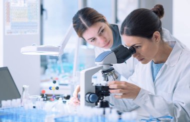Young female researchers working together in a medical lab, they are examining samples with a microscope