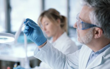 Professional researcher testing a sample in the laboratory, he is holding a test tube, medical and scientific reasearch concept