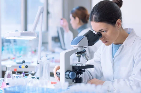 Students doing research in the clinical laboratory, a researcher is using a microscope in the foreground