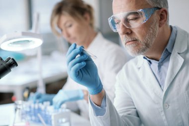 Professional researcher testing a sample in the laboratory, he is holding a test tube, medical and scientific reasearch concept