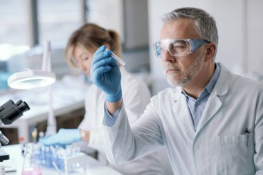 Professional researcher testing a sample in the laboratory, he is holding a test tube, medical and scientific reasearch concept