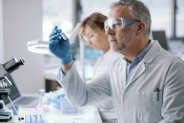 Professional researcher testing a sample in the laboratory, he is holding a test tube, medical and scientific reasearch concept