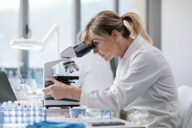 Professional female scientist working in the laboratory, she is looking through a microscope, medical research concept
