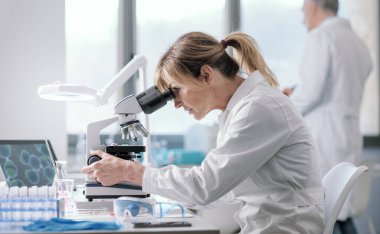 Woman working in a medical laboratory, she is using a microscope